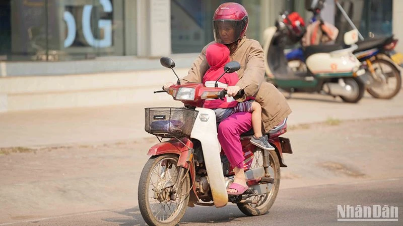 Người dân Lào tìm cách hạn chế nắng nóng khi tham gia giao thông. Ảnh: Hải Tiến
